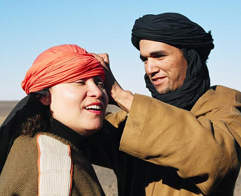 A local Berber guide helps a group member with her head scarf, Sahara Desert, Morocco.