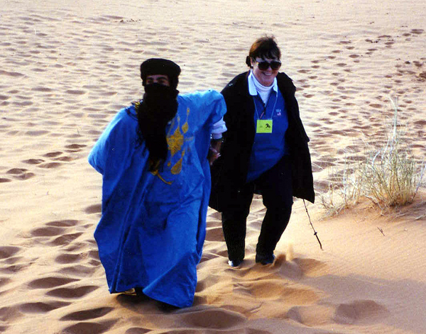 A Blueman helps a Ya'lla traveler climb a dune in the Sahara Desert of Morocco. Tuareg Berbers are known as Bluemen because of their traditional blue scarves and robes.